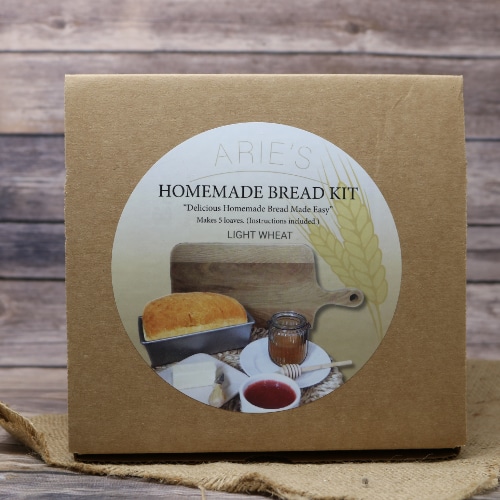 A brown box with a round logo sticker containing a complete Homemade Bread Kit on rustic burlap with a wooden background.