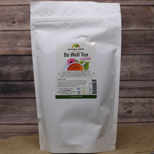 A tall white bag containing Be Well Tea on rustic burlap with a wooden background.