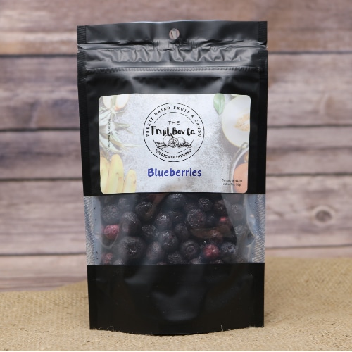 A black resealable bag with a clear window revealing Blueberries Freeze Dried on a rustic burlap with a wooden background.