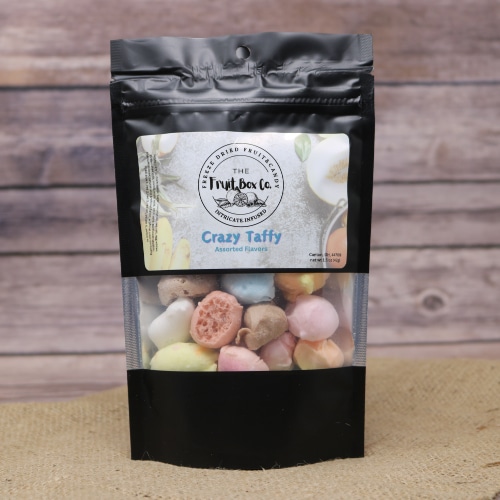 A black resealable bag with a clear window revealing Crazy Taffy Freeze Dried on a rustic burlap with a wooden background.