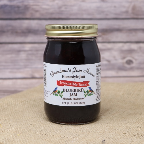 A pint jar of Grandma's Bluebird Jam which is a combination of rhubarb and blueberries on rustic burlap with a wooden background.