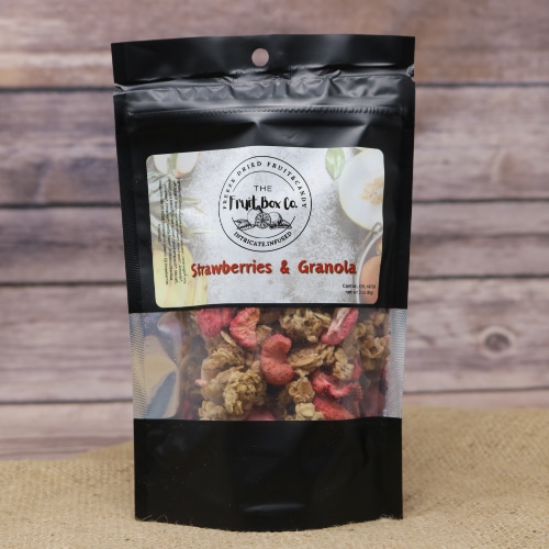A black resealable bag with a clear window revealing Strawberries And Granola Freeze Dried on a rustic burlap with a wooden background.