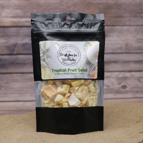 A black resealable bag with Tropical Fruit Salad Freeze Dried which is a blend of pineapple, mango, papaya and coconut, on a rustic burlap with a wooden background.