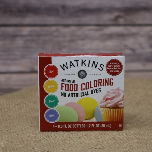 A small box containing four bottles of Watkins Food Coloring assorted colors no artificial dyes on rustic burlap with a wooden background.