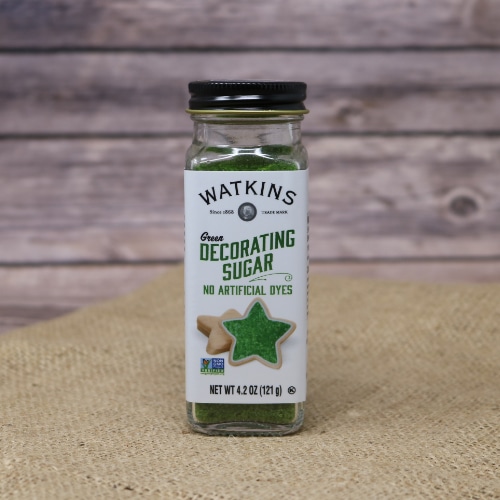 A small glass shaker container with a removable lid of Watkins Green Decorating Sugar, these sprinkles have no artificial dyes, on rustic burlap with a wooden background.