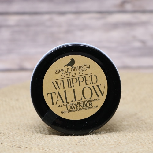 A small glass container of Whipped Beef Tallow Lavender on rustic burlap with a wooden background.