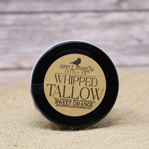 A small glass container of Whipped Beef Tallow Sweet Orange on rustic burlap with a wooden background.