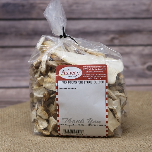 A clear plastic bag of Mushrooms Shiitake Sliced sealed with a black twist tie on rustic burlap with a wooden background.