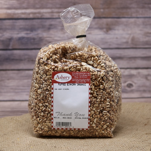 A clear bag of Puffed Einkorn Organic sealed with a black twist tie on rustic burlap with a wooden background.