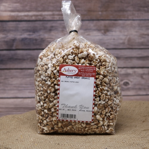 A clear bag of Puffed Wheat Organic sealed with a black twist tie on rustic burlap with a wooden background.