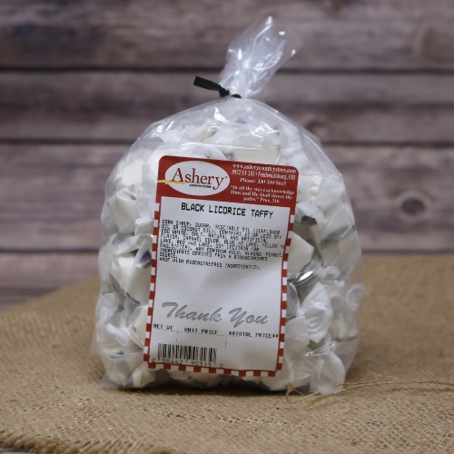 A clear plastic bag sealed with a black twist tie of Black Licorice Taffy on rustic burlap with a wooden background.