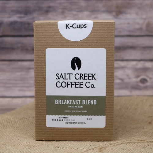 A brown box containing 12 Breakfast Blend Coffee K-Cups on rustic burlap with a wooden background.