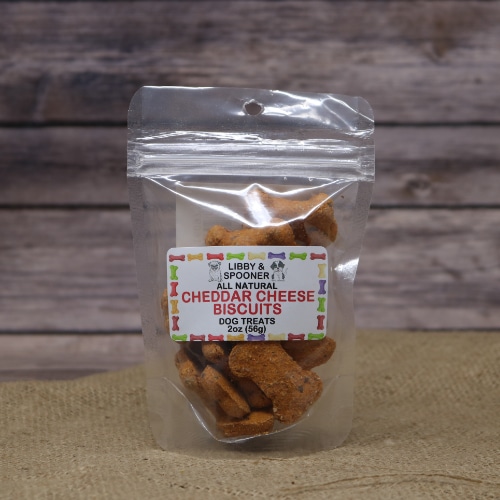 A small resealable plastic bag containing Cheddar Cheese Dog Biscuits 2 oz on rustic burlap with a wooden background.
