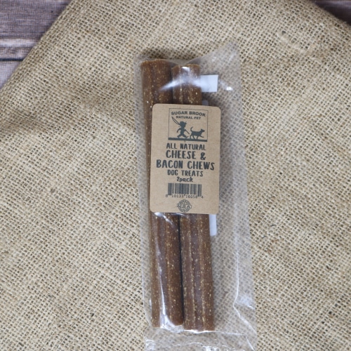 A thin plastic package containing 2 Cheese Bacon Dog Chews on rustic burlap with a wooden background.