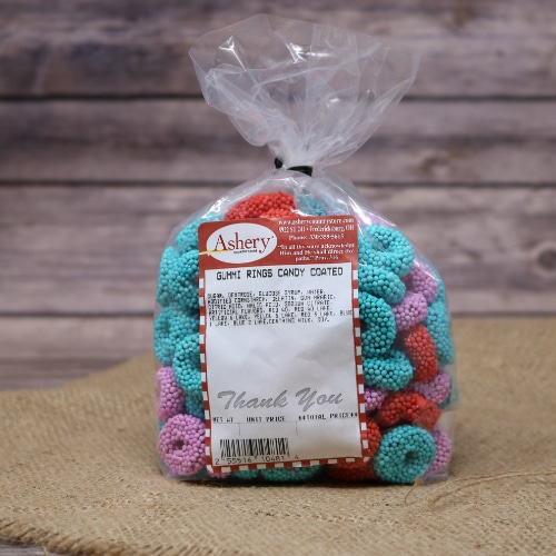 A clear plastic bag sealed with a black twist tie containing blue, red and purple Gummi Rings Candy Coated on rustic burlap with a wooden background.