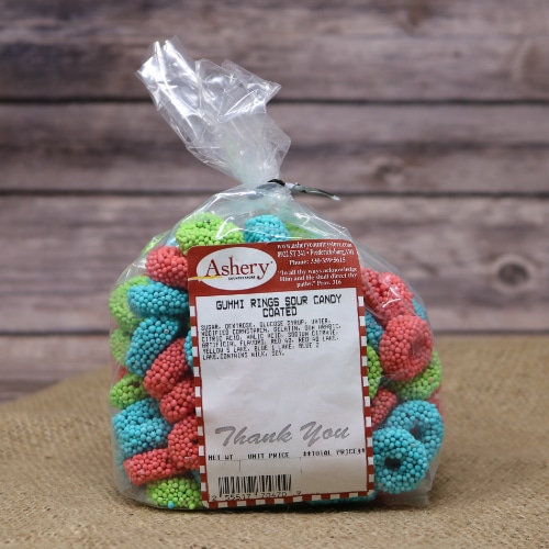A clear plastic bag sealed with a black twist tie containing colorful Gummi Rings Sour Candy Coated on rustic burlap with a wooden background.