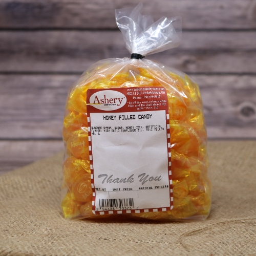 A clear plastic bag sealed with a black twist tie containing wrapped Honey Filled Candy on rustic burlap with a wooden background.