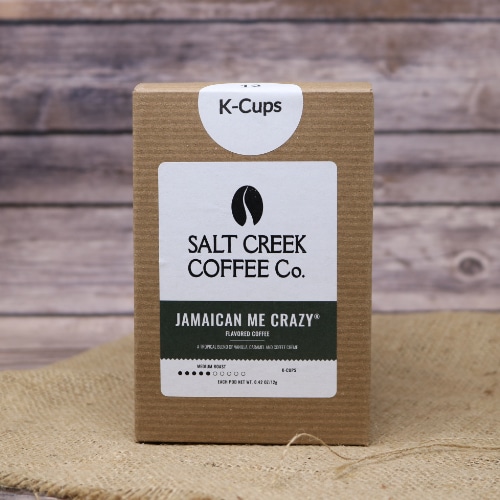 A brown box with a dark green label containing 12 Jamaican Me Crazy Coffee K-Cups on rustic burlap with a wooden background.