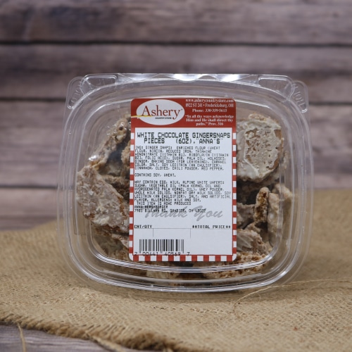A clear container of White Chocolate Gingersnap Pieces on rustic burlap with a wooden background.