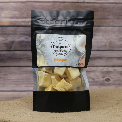 A black bag with a clear window revealing Freeze Dried Mangos on a rustic burlap with a wooden background.