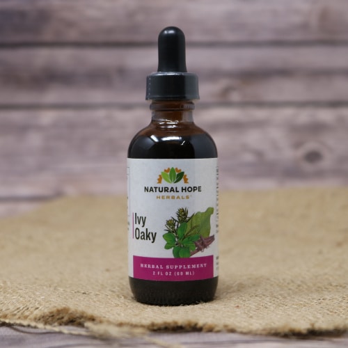 A small glass bottle with a squeeze dropper of Ivy Oaky which is an immune tonic of herbs for the skin, on rustic burlap with a wooden background.