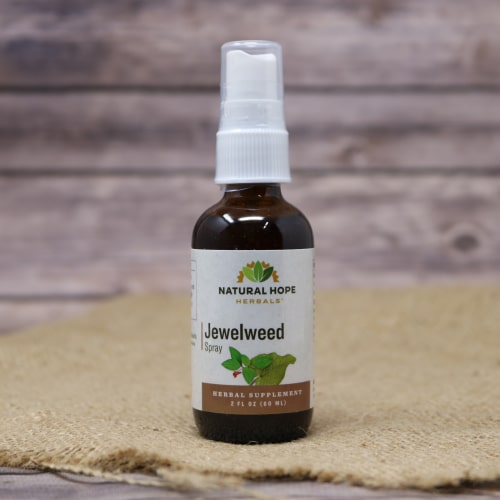 A small glass spray bottle with Jewelweed Spray displayed on rustic burlap with a wooden background.