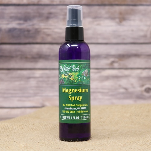 A purple spray bottle with a green label of Wild Erb Magnesium Spray on rustic burlap with a wooden background.